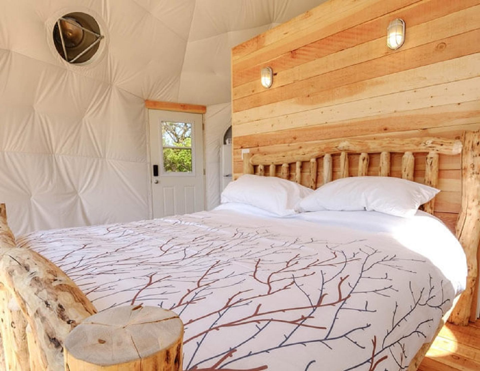 Cozy glamping dome interior with wooden bed frame and bright natural light.