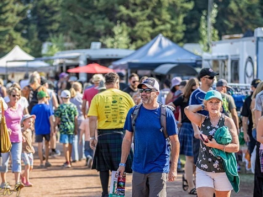 Crowd of people walking through an outdoor market with tents and vendor stalls.