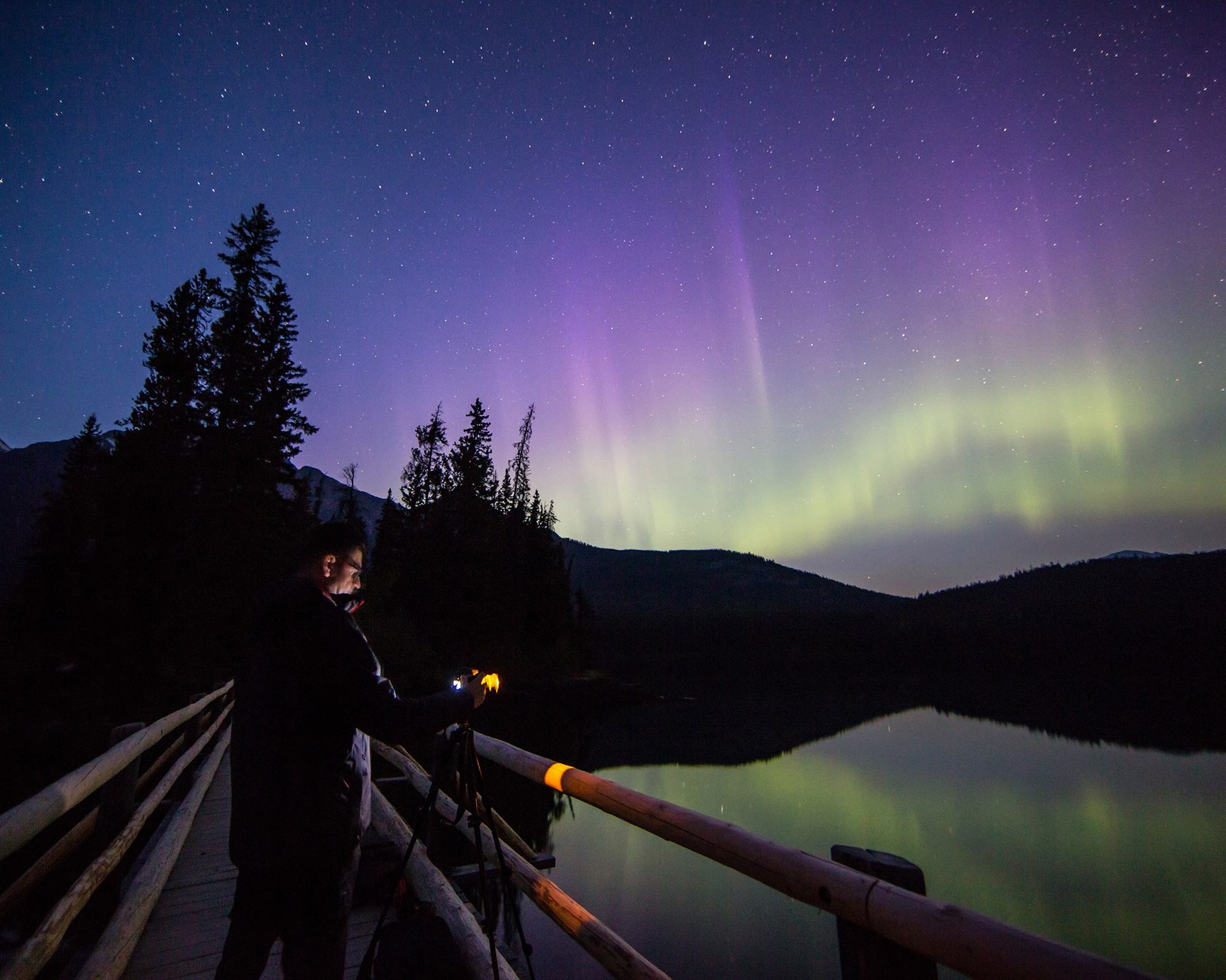 A photographer capturing the northern lights on a bridge at night, with stars in the sky.