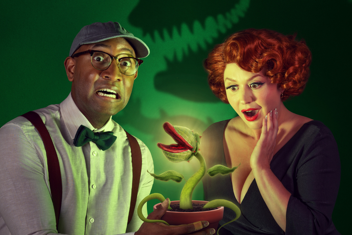 Two people stare at a glowing, open-mouthed carnivorous plant in a pot.