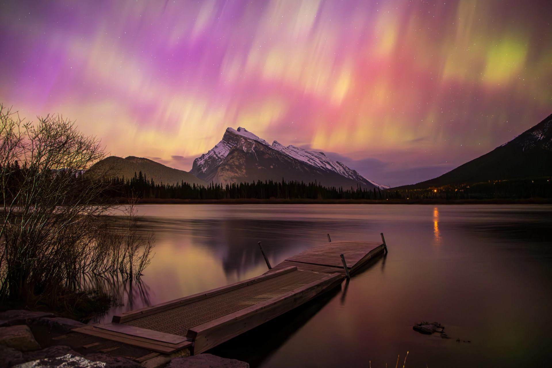 Aurora lights over a calm lake with snow-capped mountains in Jasper National Park.
