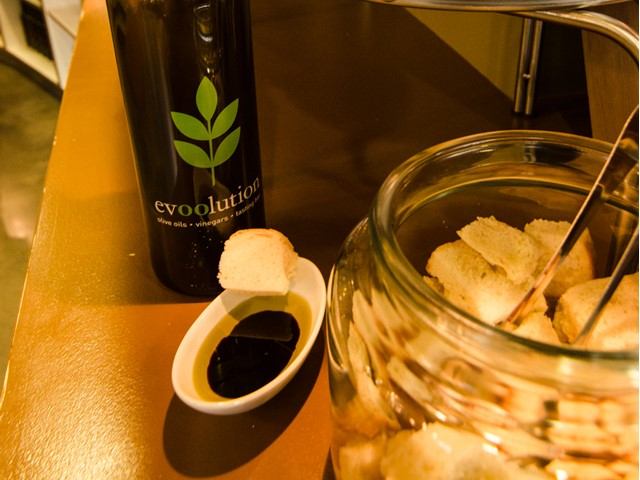 evoolution bottle and small dish of dark sauce beside glass jar with bread pieces on table.