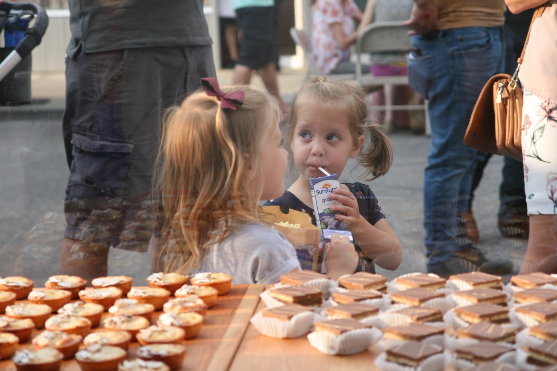 Young girls drink juice and look at baked goods through a glass display.
