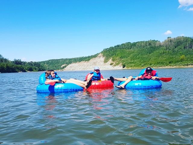 Three people float in tubes on a lake with hills and blue sky in the background.