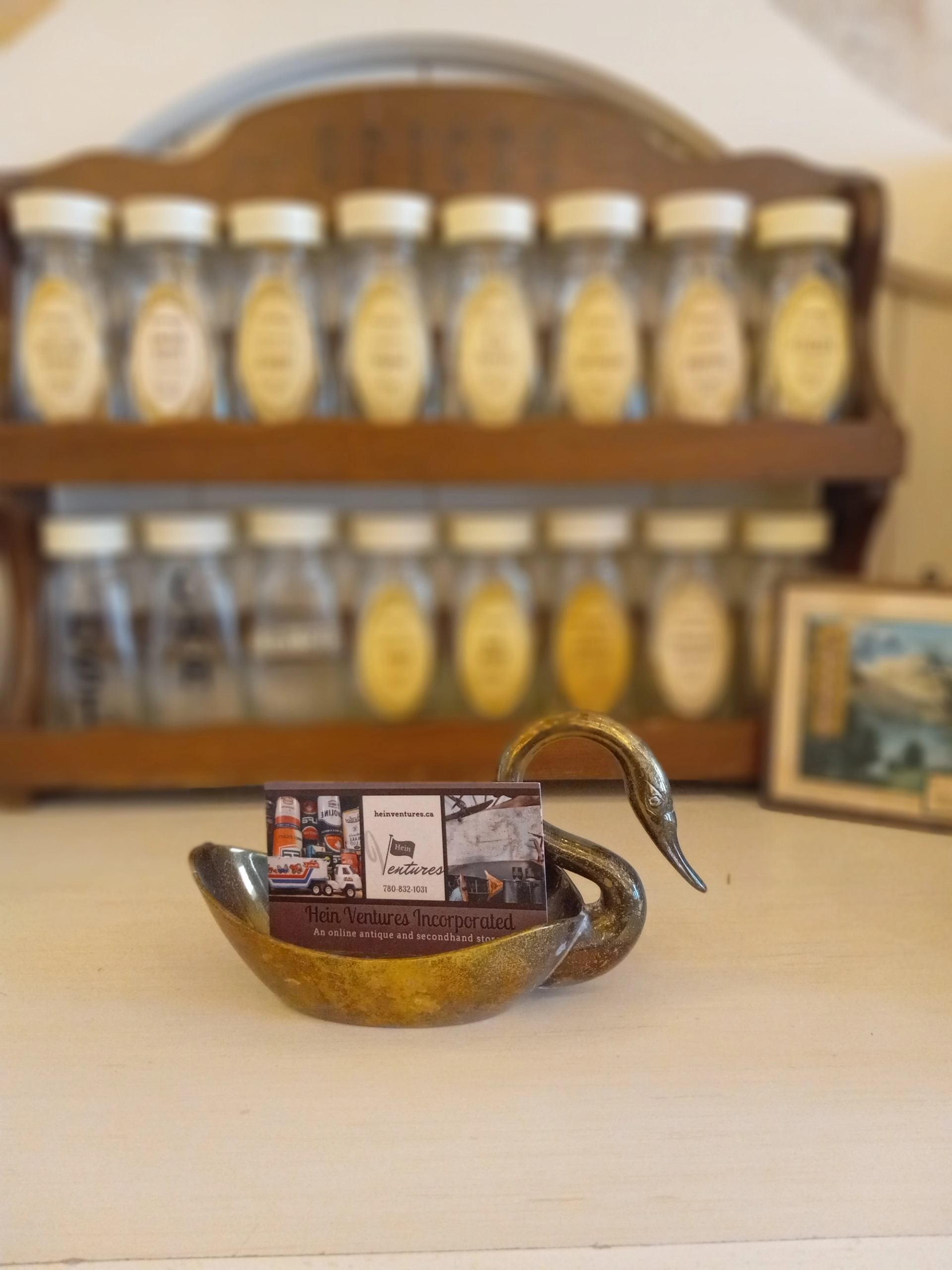 Brass swan-shaped dish holding cards, with spice jars arranged on a wooden rack in the background.