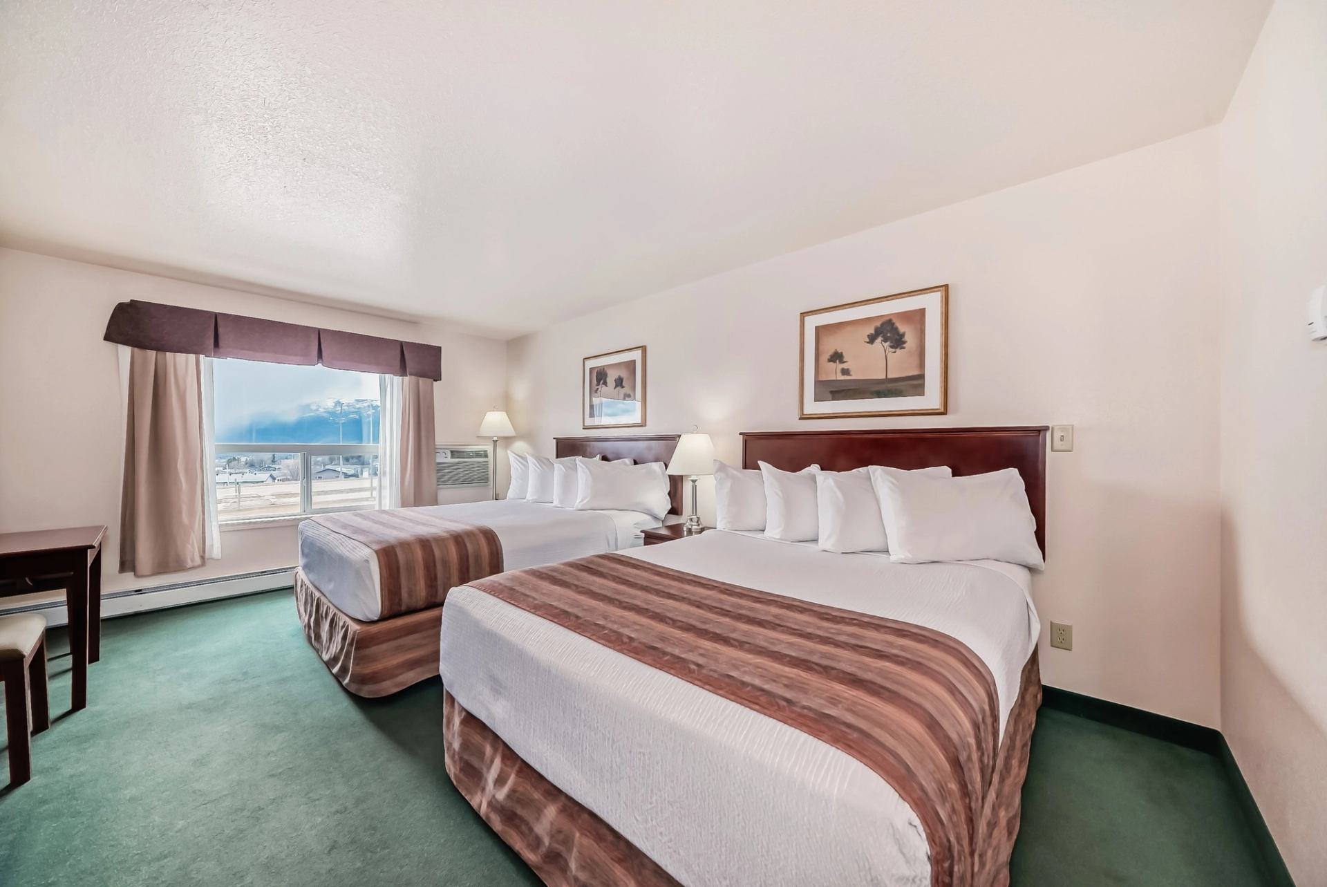 Hotel room with two queen beds, desk, and large window showcasing scenic mountain views.