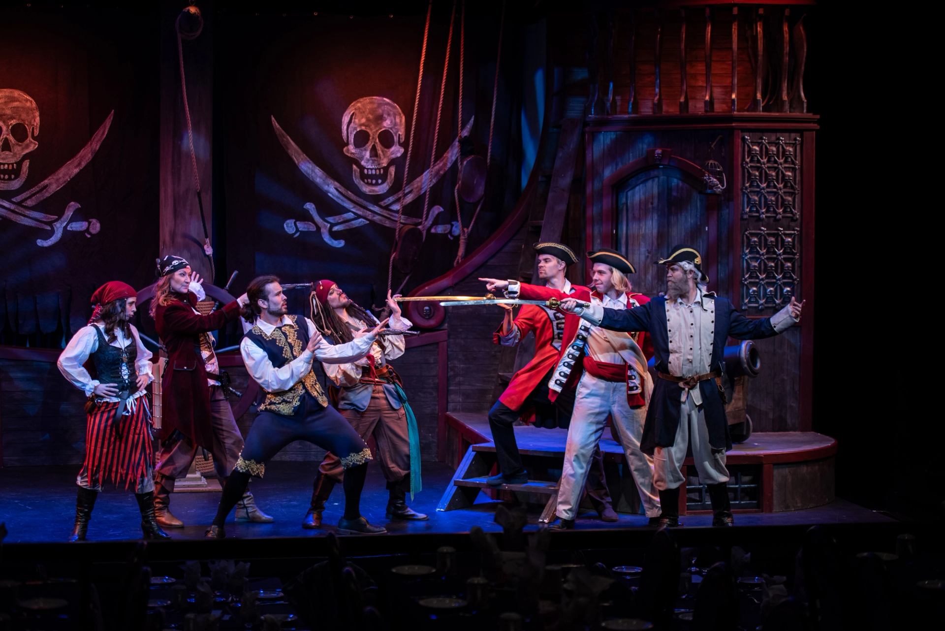 Pirate cast on stage holding swords in front of skull backdrop and wooden ship set.