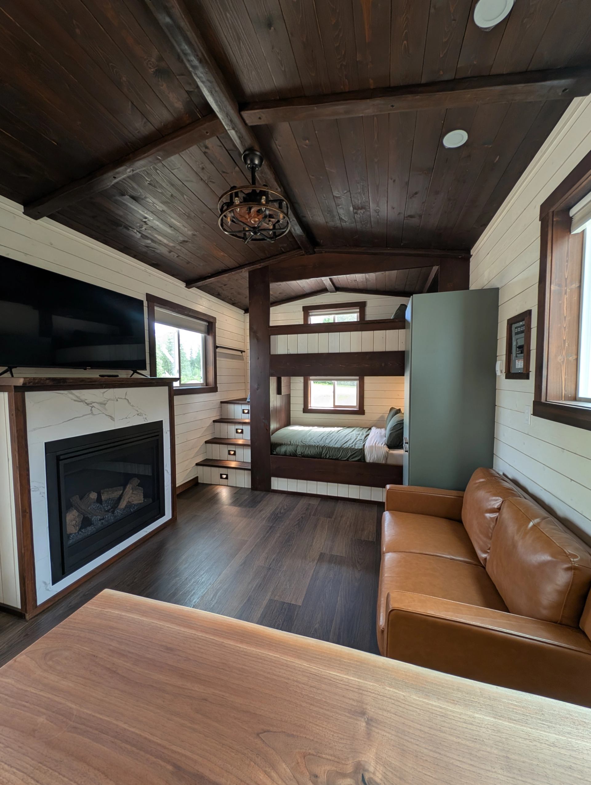 Cabin interior with bunk beds, fireplace, television, leather sofa and wood ceiling.