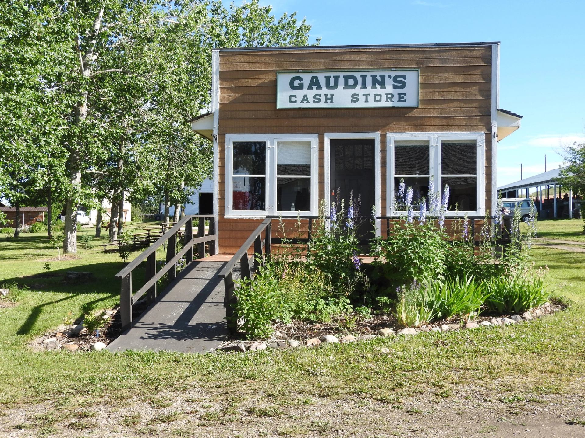 Historic building with “GAUDIN’S CASH STORE” sign, front windows, and garden flowers.