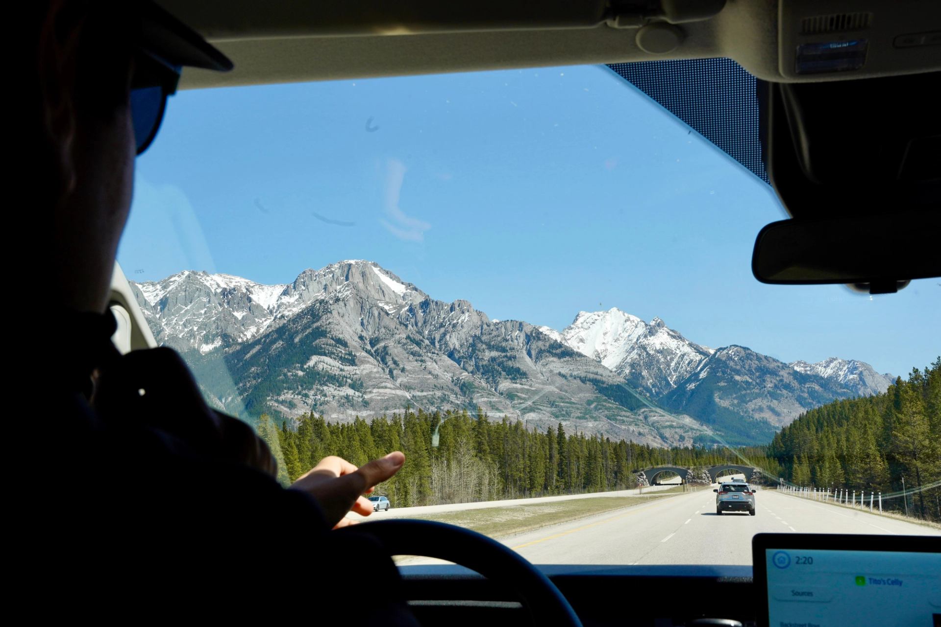 Person in a vehicle looking out at a highway leading toward snowy mountain peaks.
