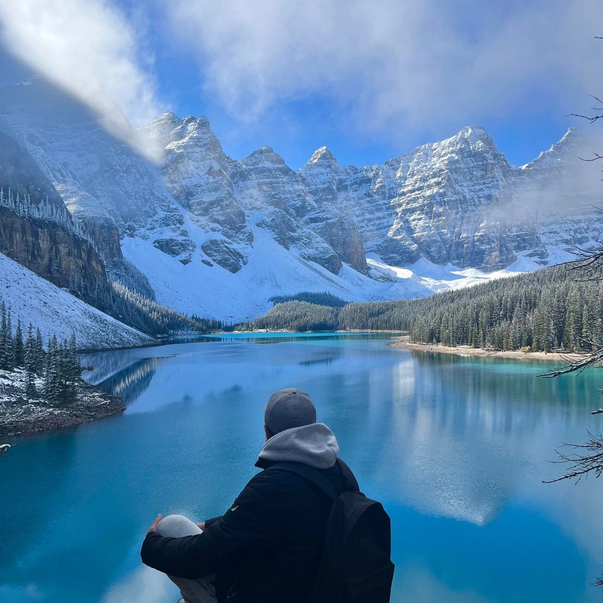 Man sitting facing the Valley of 10 Peaks with the bright blue Moraine Lake beneath