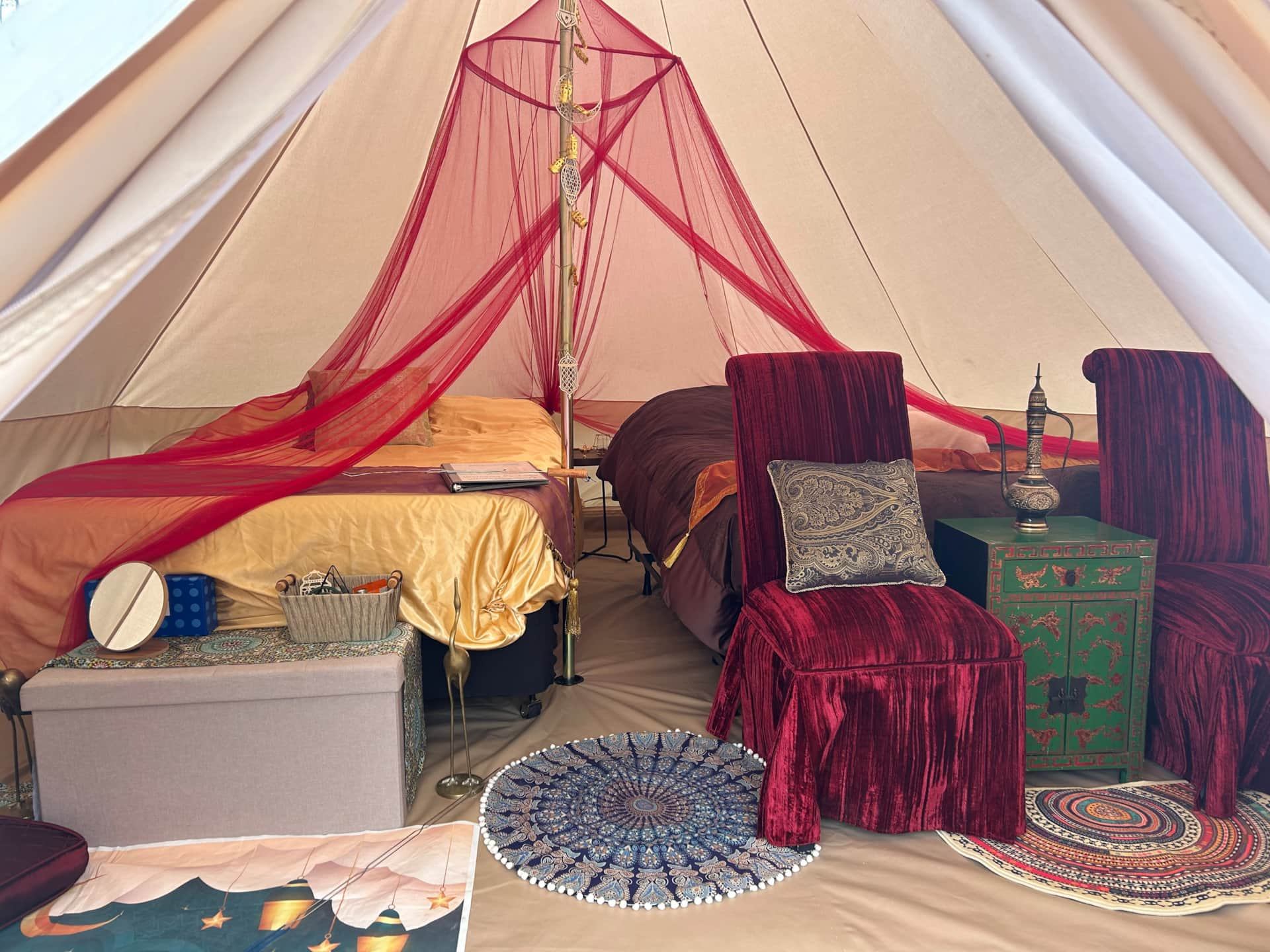 Elegant tent interior with red canopy, plush chairs, and decorative rugs