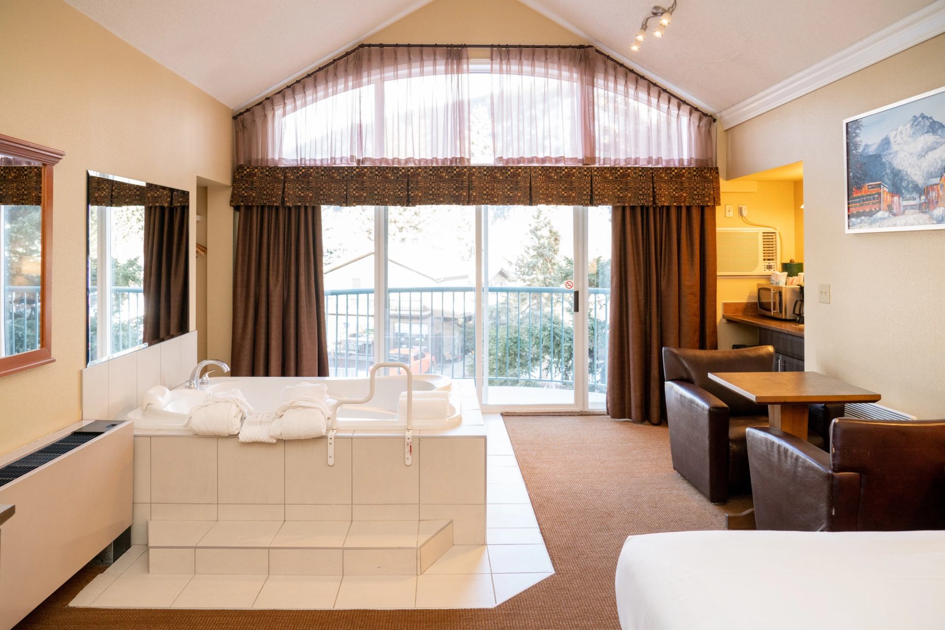 Hotel room with jacuzzi tub, seating area, and large windows with sheer curtains.