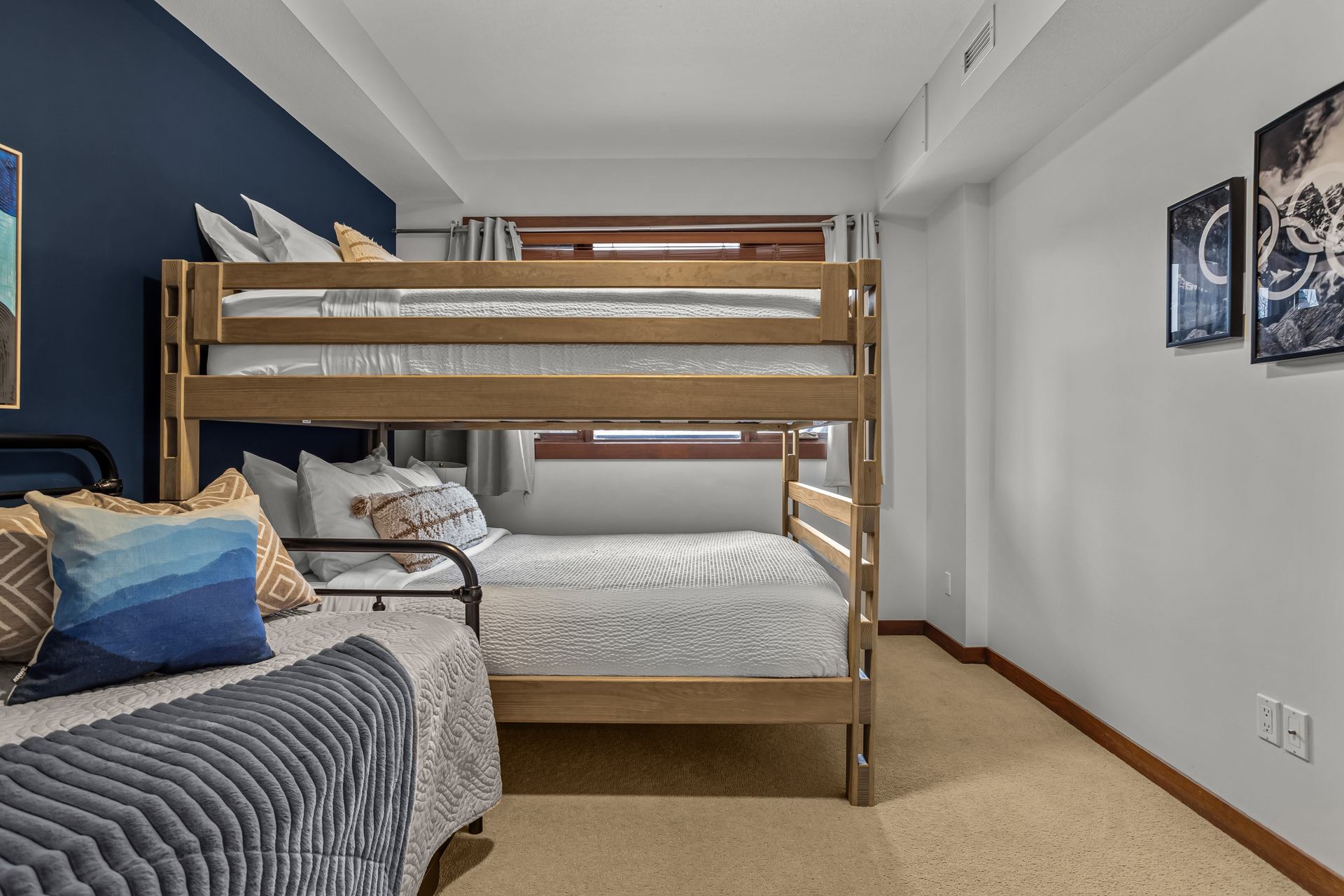 Bedroom with wooden bunk bed, daybed, blue accent wall and window with curtains.