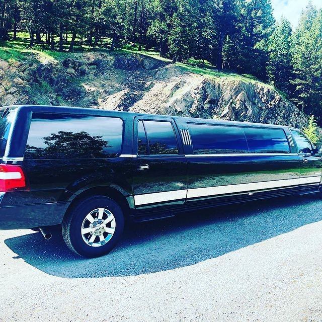 Long black Quest Limos limousine parked roadside with forest and rocky hillside in the background.