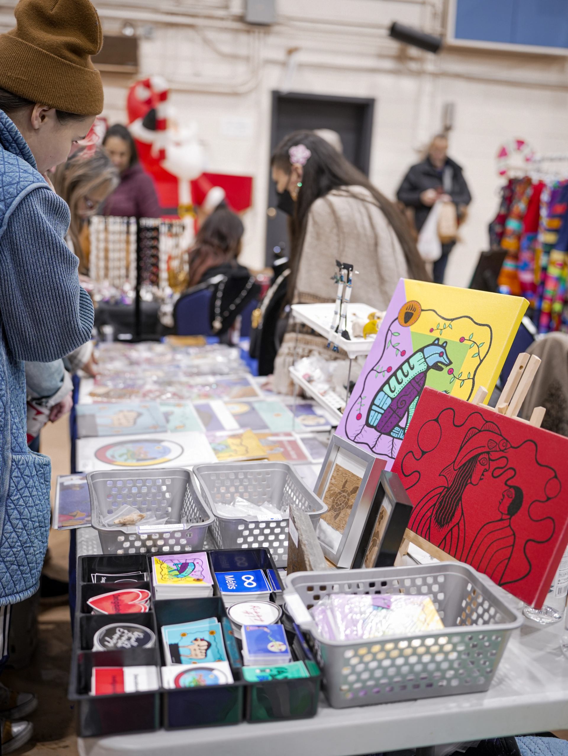 Table with baskets, prints, and shoppers at a lively holiday market.