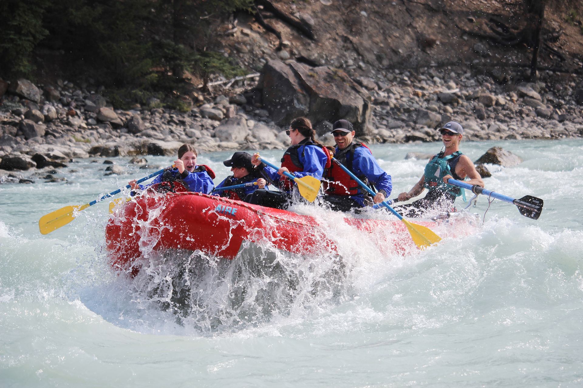 Red raft charging through choppy whitewater as the group paddles downstream.