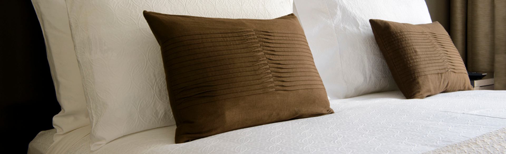 A neatly made bed features plush white linens and decorative accent pillows in a bright guest room.