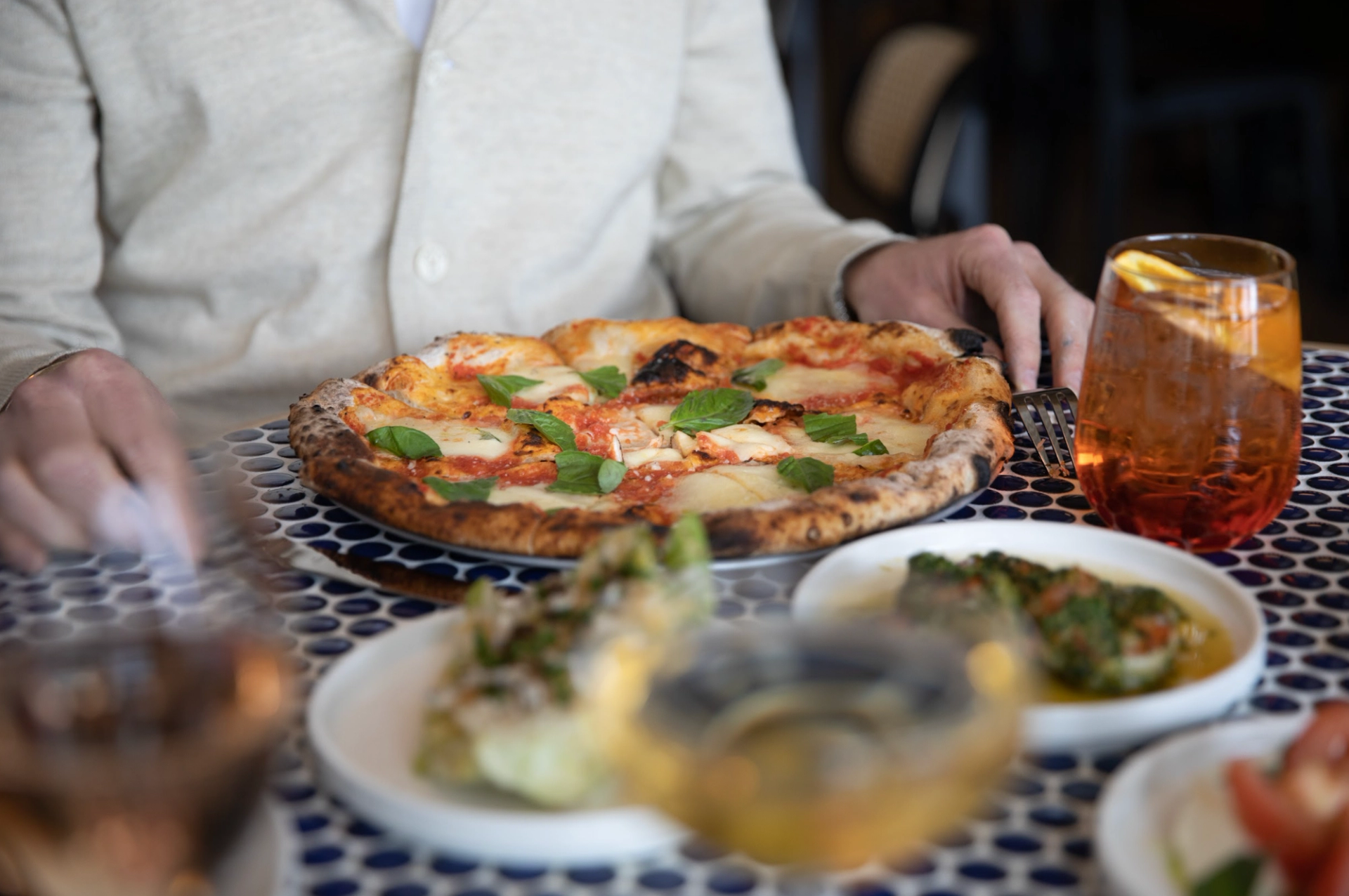 Close‑up of a pizza and drinks on a patterned table.