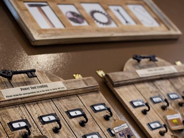 Wooden boards with numbered hooks are displayed against a brown wall, labeled "Power Tool Lending" for organizing tool keys, under framed tool images.
