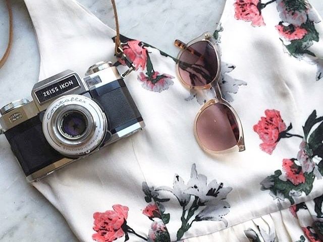 Vintage camera, sunglasses, and floral fabric with red and black flower patterns on a surface.