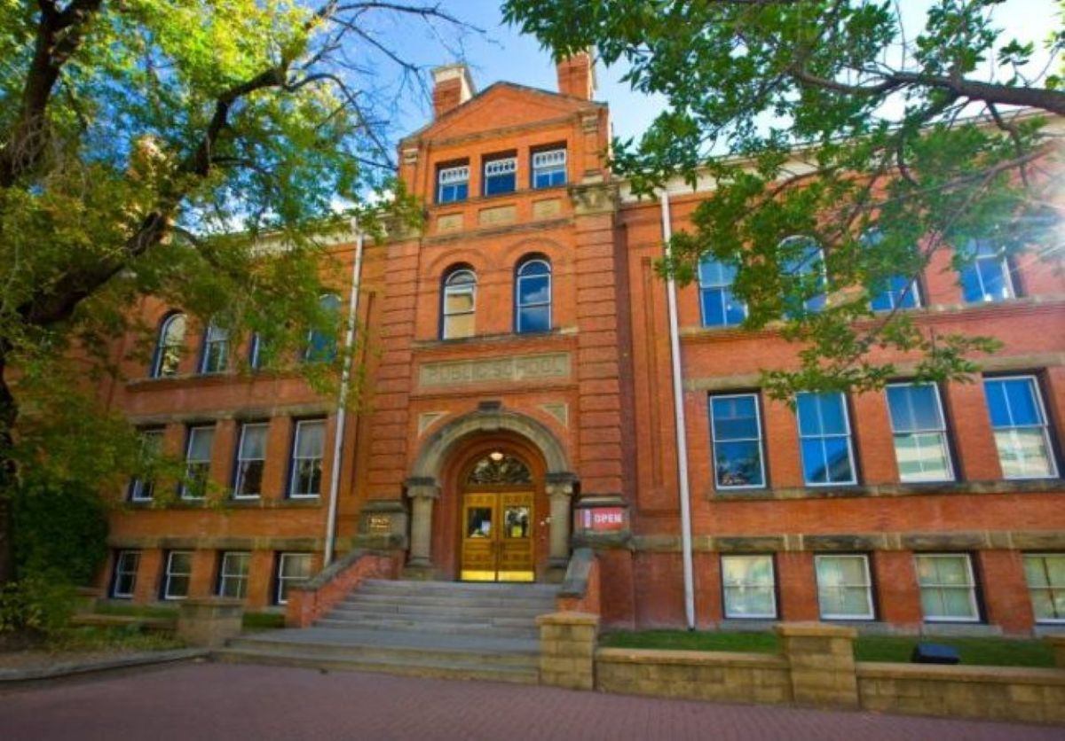 Historic red brick building with arched entrance, large windows and trees framing the facade.