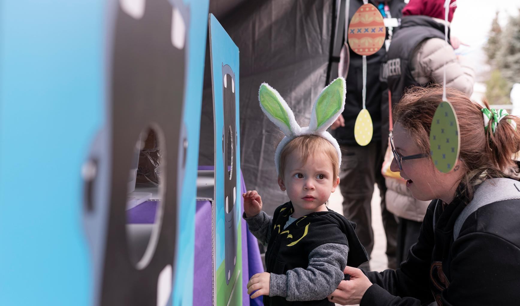 Child wearing bunny ears exploring a blue activity booth with egg decorations