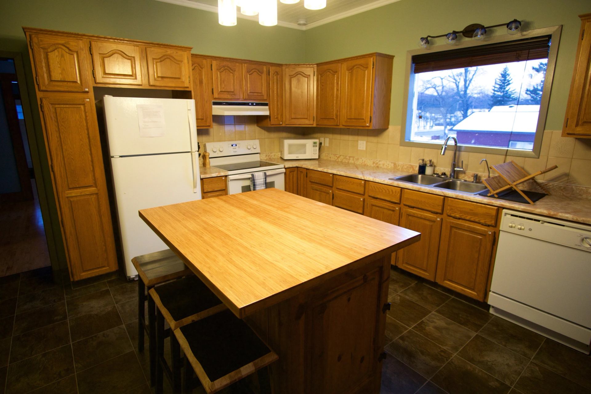 Kitchen with wooden cabinets, center island, and white appliances under warm lighting.