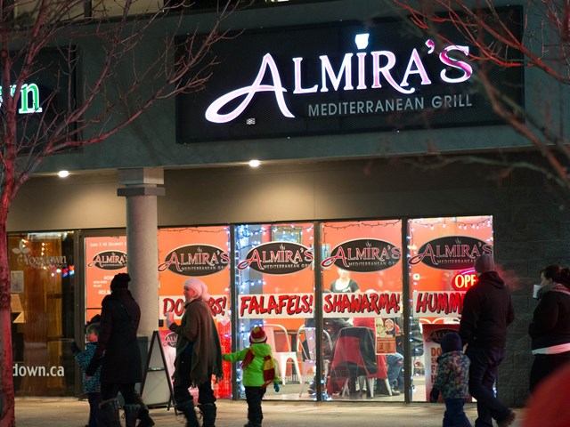 Night view of Almira's Mediterranean Grill with illuminated sign and people outside.