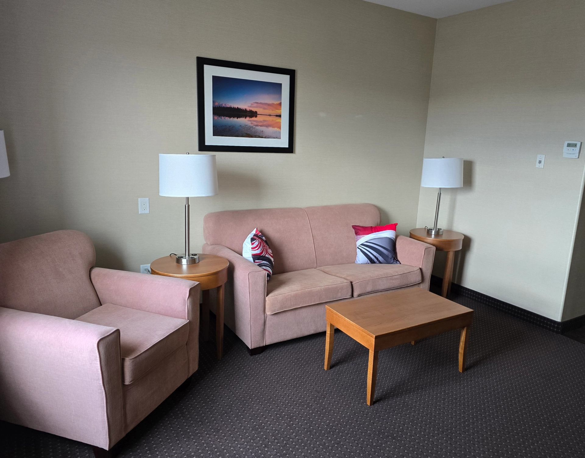 Hotel lounge seating area with pink couch, chairs, tables, and framed wall art.