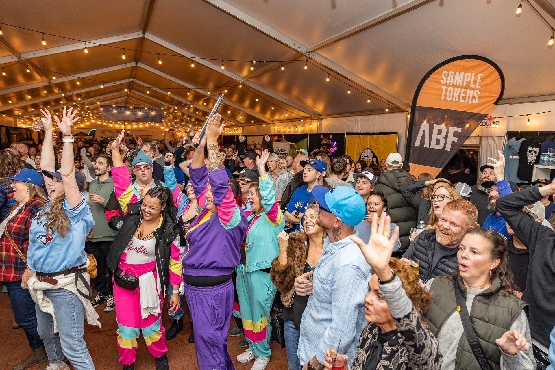 Crowd inside festival tent raises hands under string lights near Sample Tokens banner.