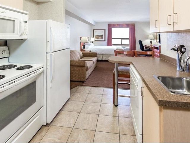 Hotel suite with small kitchen, sofa, desk and bed in open-plan layout.