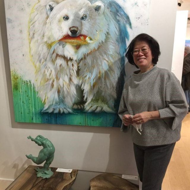 Person stands beside painting of white bear holding a fish; small sculpture below.