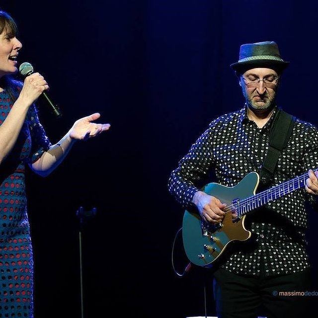 Singer with microphone and guitarist in hat playing electric guitar onstage.