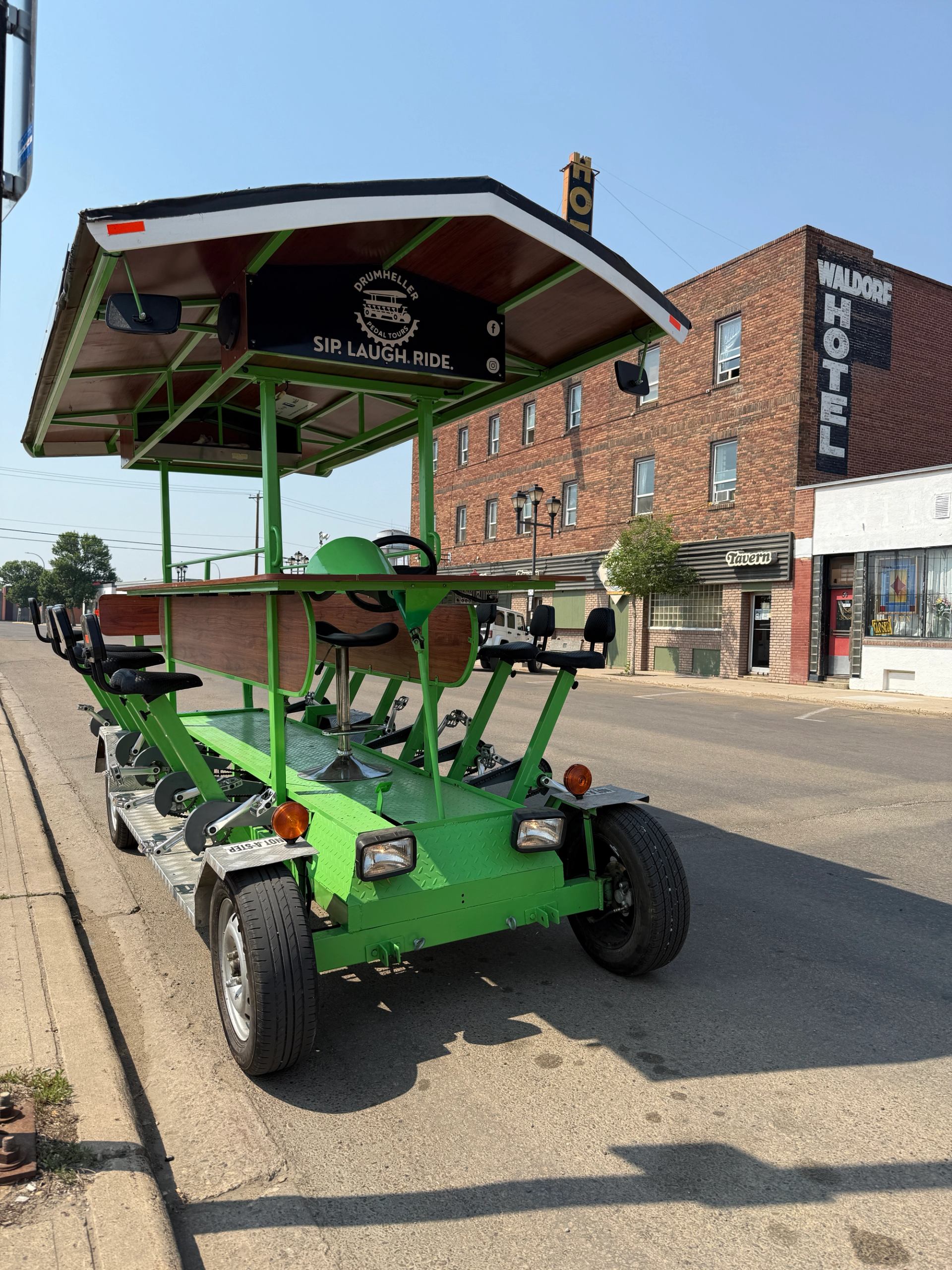 The empty green pedal-powered party trolley parked on the side of the street.