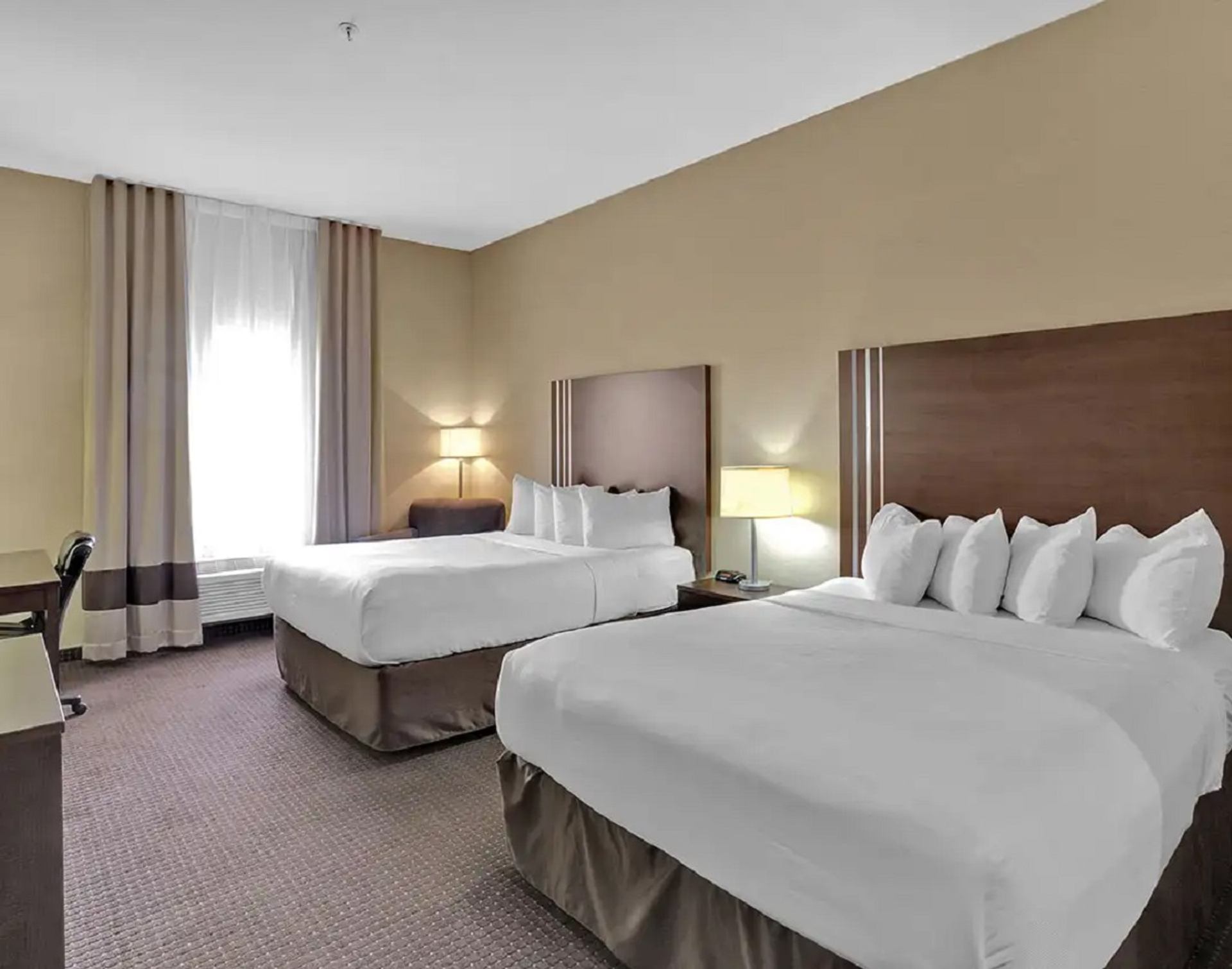 Hotel room with two queen beds, desk, and soft lighting.