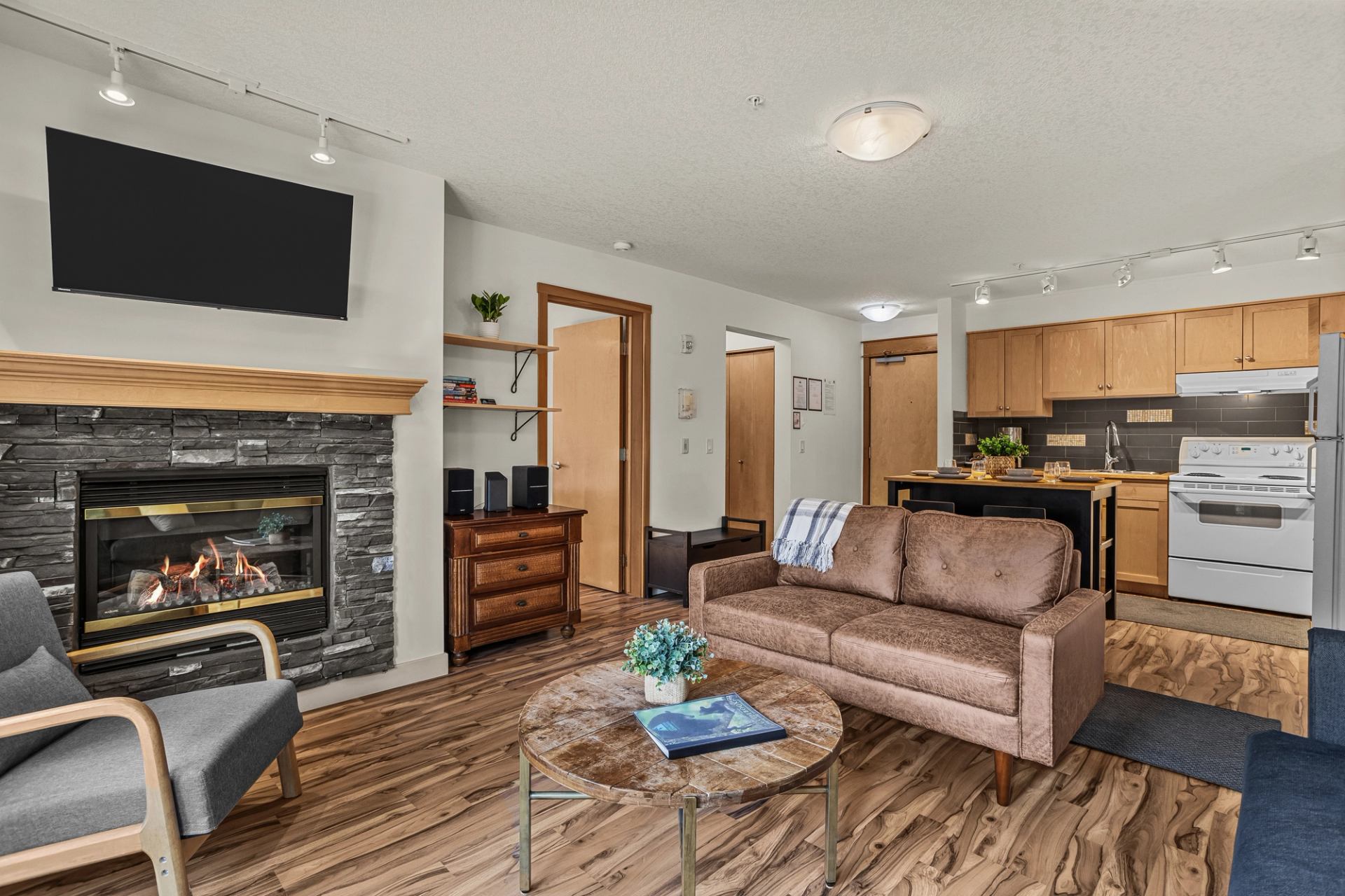 Open-concept living room with fireplace, sofa, television and wood-cabinet kitchen.