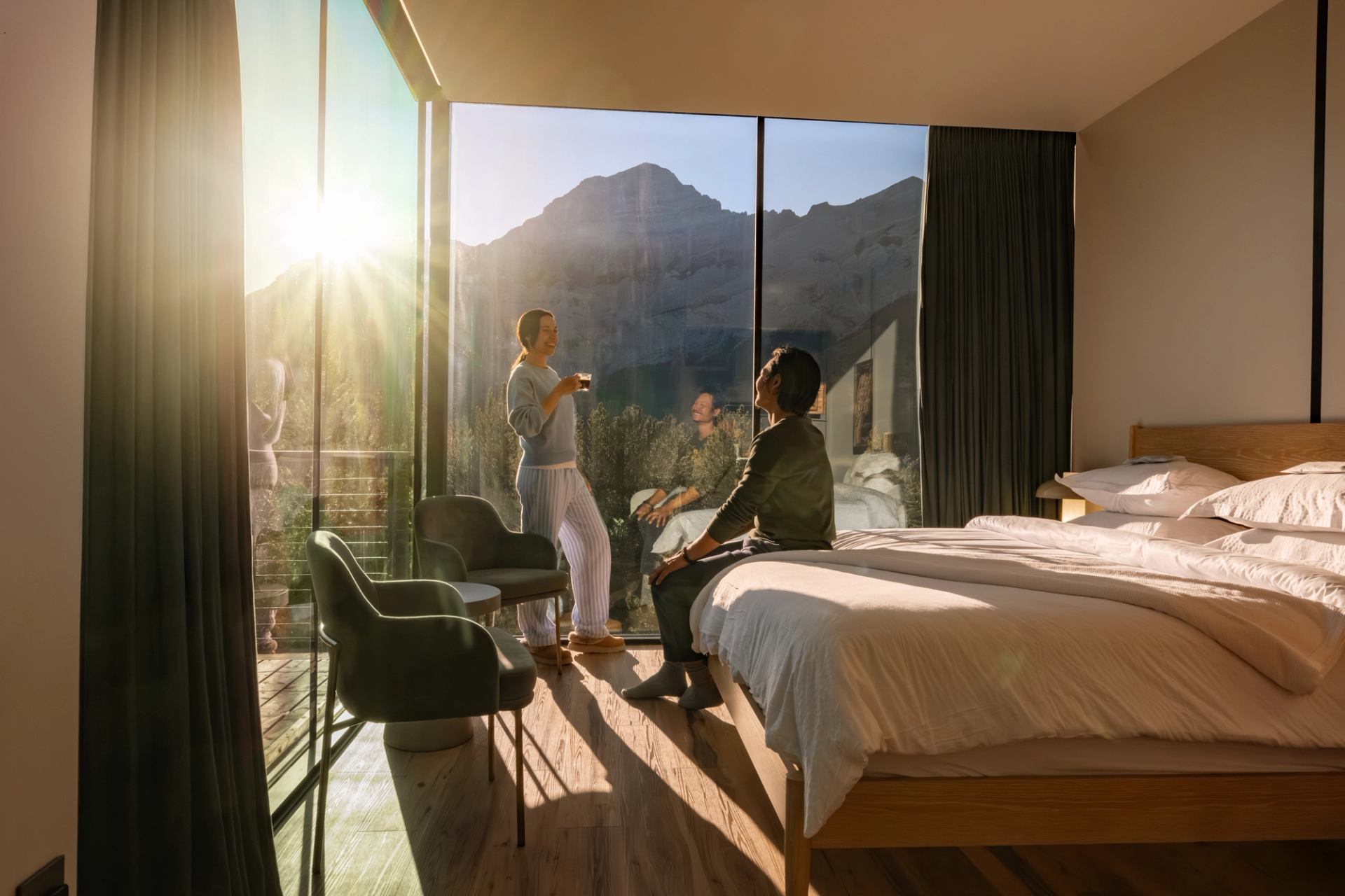 Modern glamping cabin with glass walls overlooking forest and mountains at sunset.