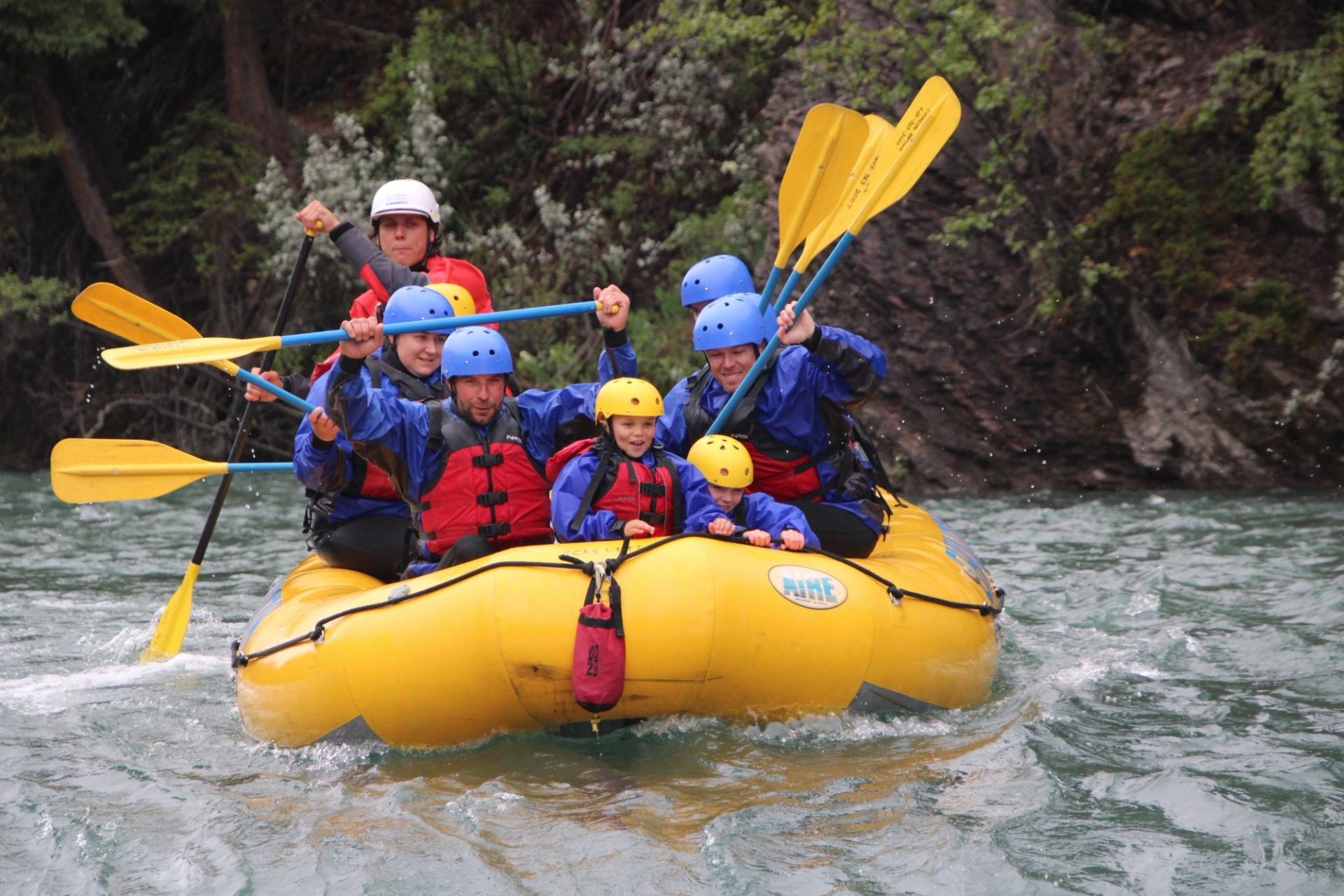 Group in helmets and lifejackets paddles yellow raft through fast river.