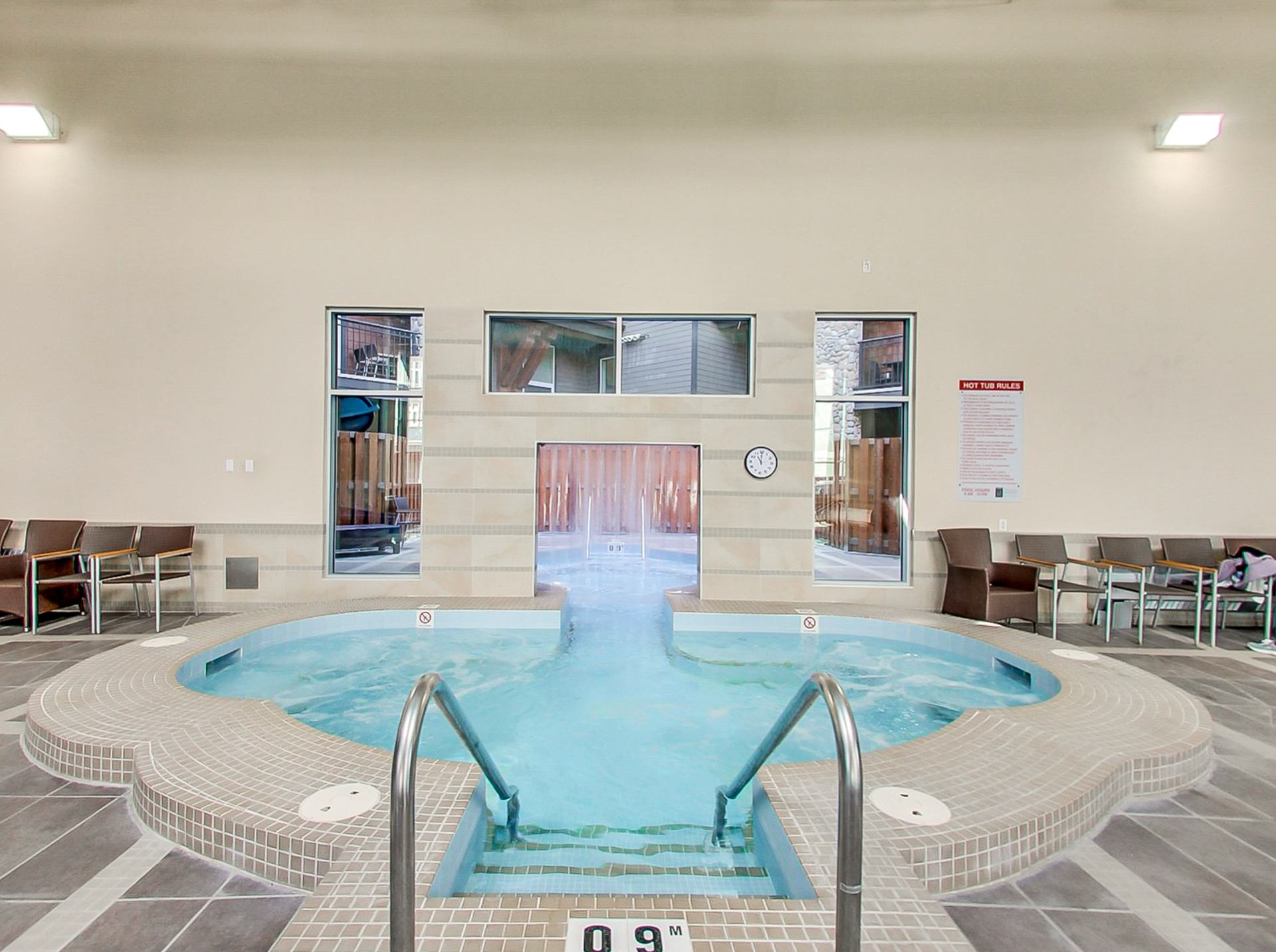 Indoor hot tub with tiled steps, metal handrails and chairs along the walls.
