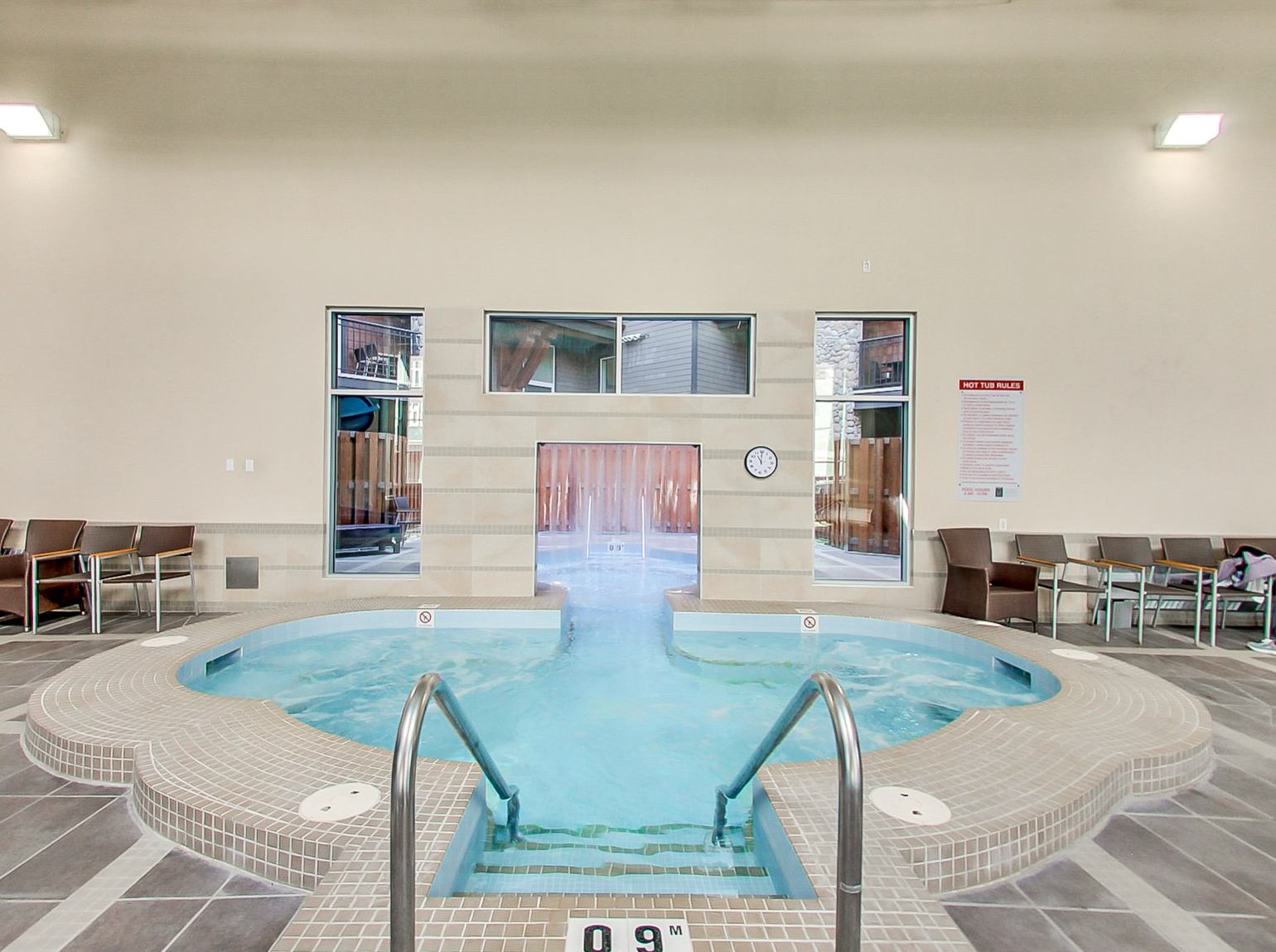 Indoor hot tub with tiled steps, metal handrails and chairs along the walls.