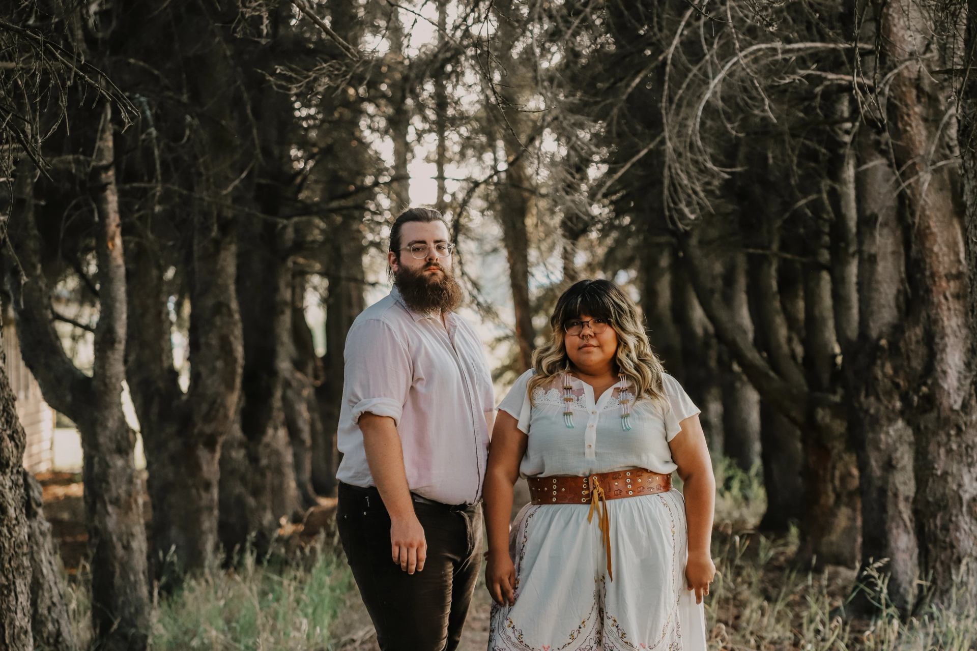 Brianna Lizotte and Ethan Graves stand in a forest, dressed for a Metis music and dance event.