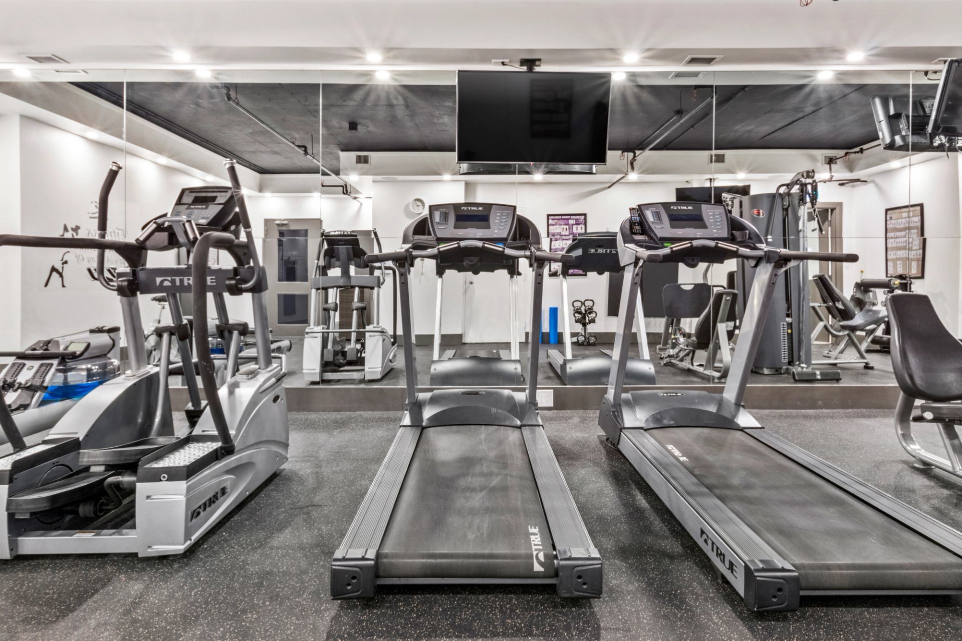 Modern fitness room with treadmills, ellipticals, weight machines and wall mirrors.