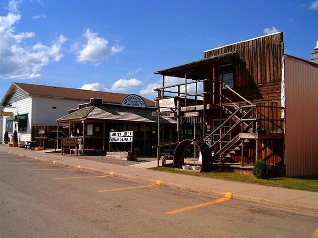 Jimmy Jock Boardwalk storefronts and wooden waterwheel beside a paved street in town.