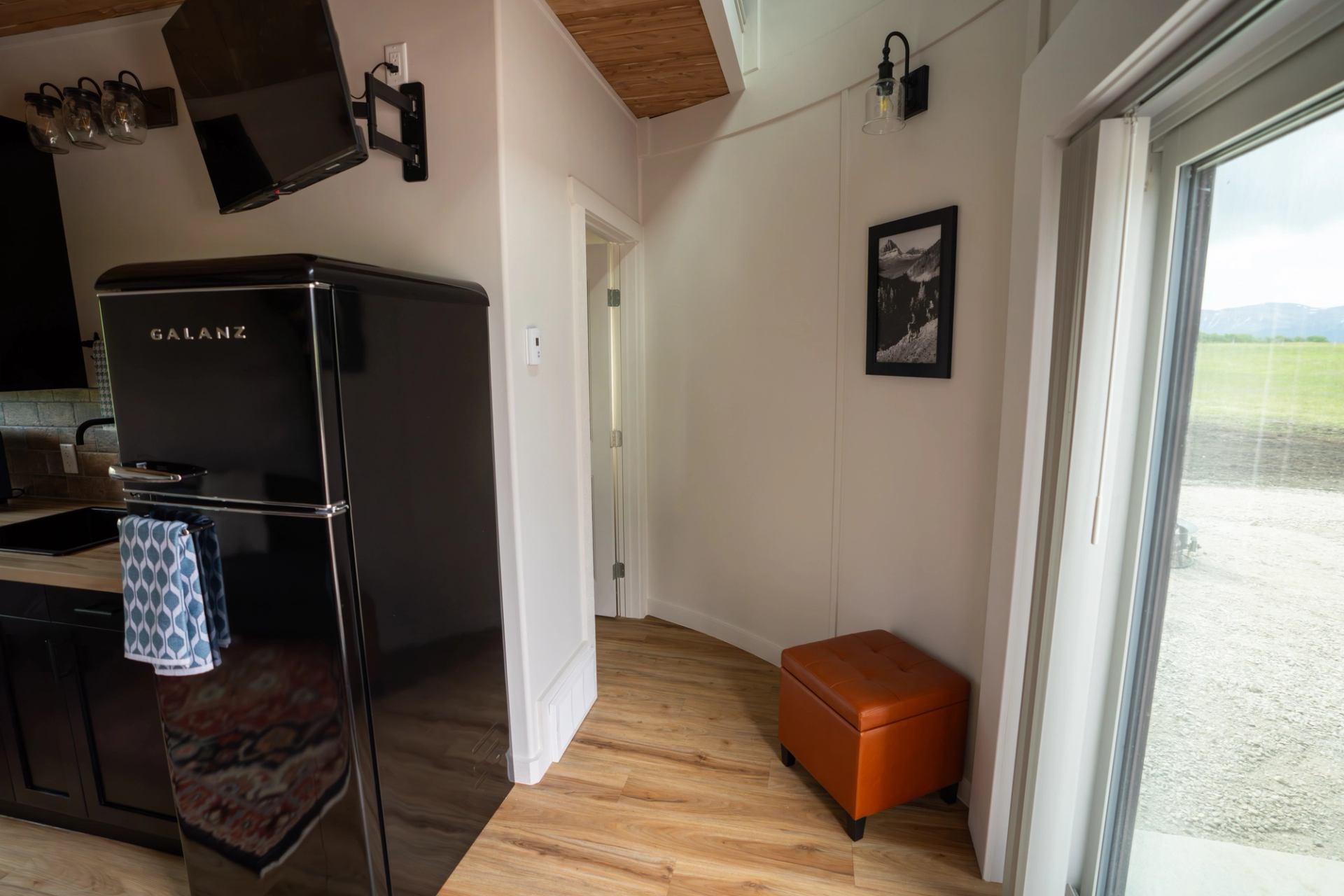 Twin Butte Silos entryway with black fridge, orange ottoman, and bright natural light.