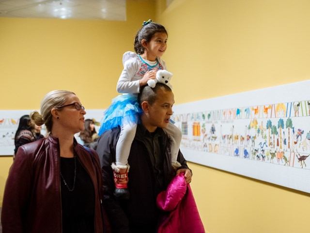 A young girl sits on her father's shoulders with her mother nearby.