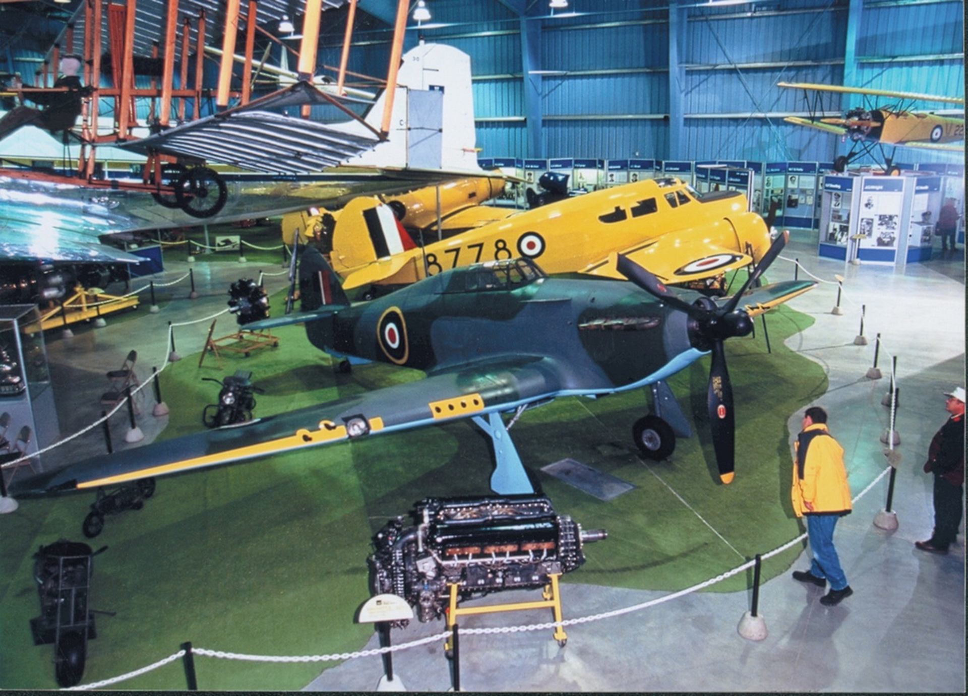 Visitors view vintage military aircraft and engines displayed inside a large aviation museum.