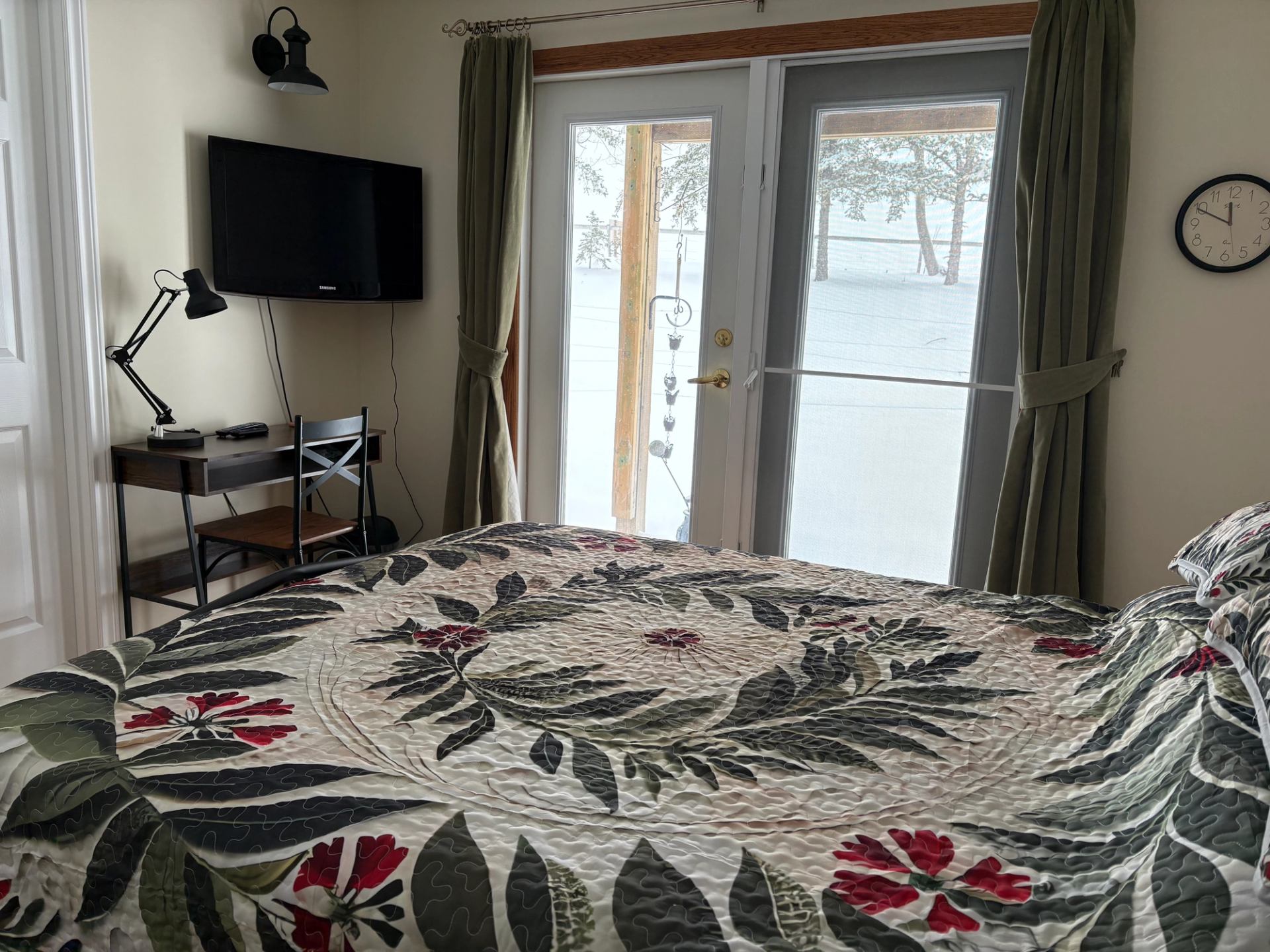 Bedroom with floral bedspread, desk and TV, glass doors showing snowy yard.