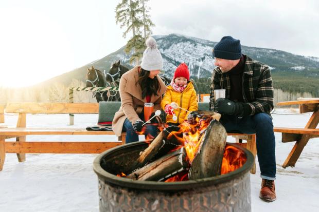 A family roasting marshmallows over a fire after a sleigh ride at Banff Trail Riders.