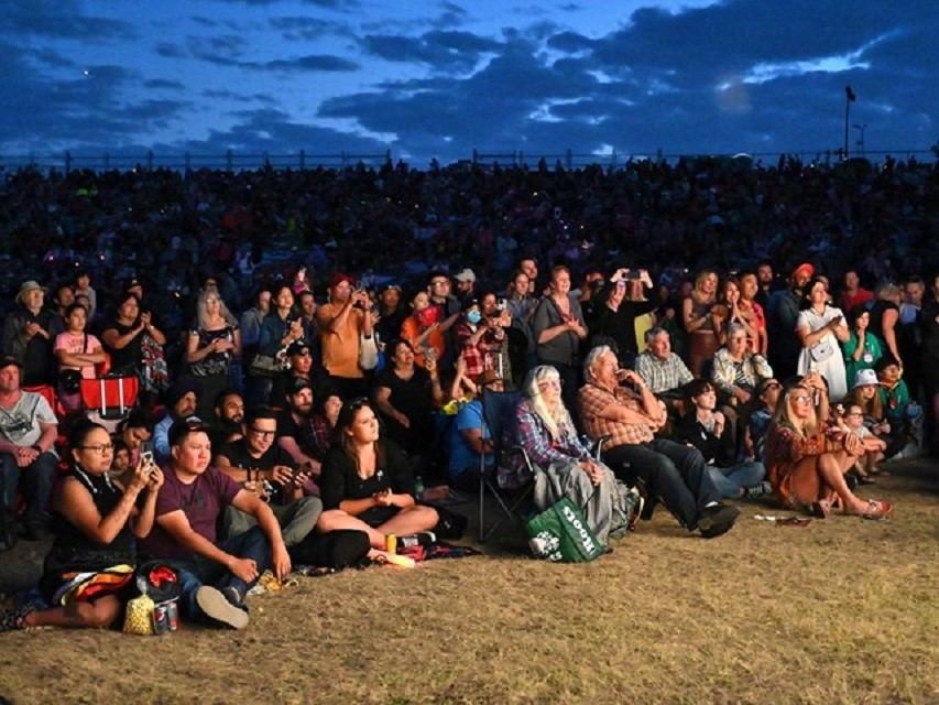 Audience seated on grass at GlobalFest, with lights and night sky in background.